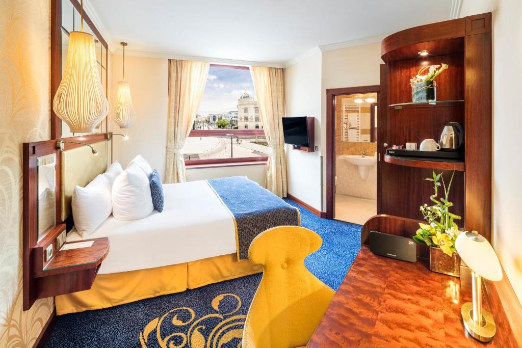 Quarto do Occidental Praha Wilson, em Praga, com cama branca, poltrona amarela e vista urbana pela janela
