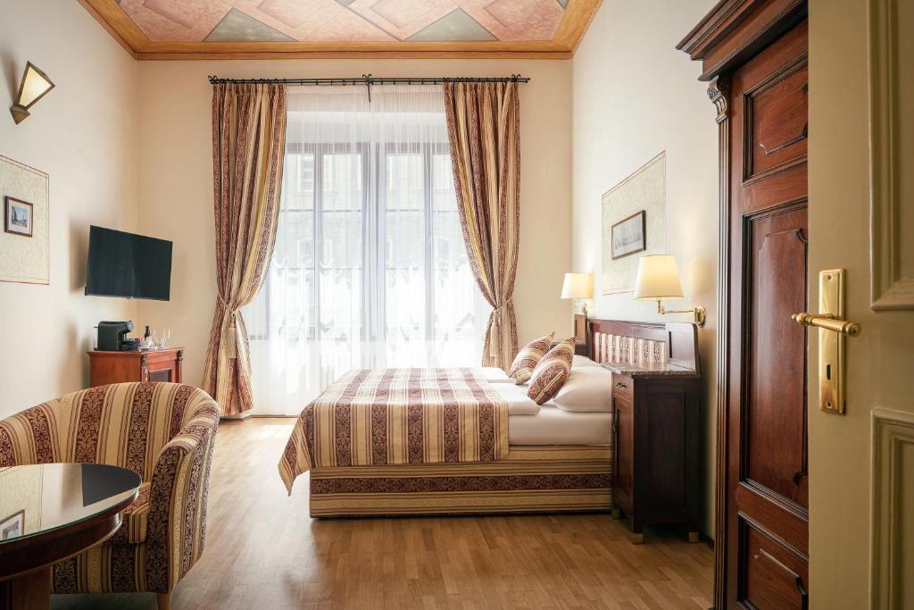 Quarto do The Charles, em Praga, com cama estampada, poltrona e janelas altas com cortinas
