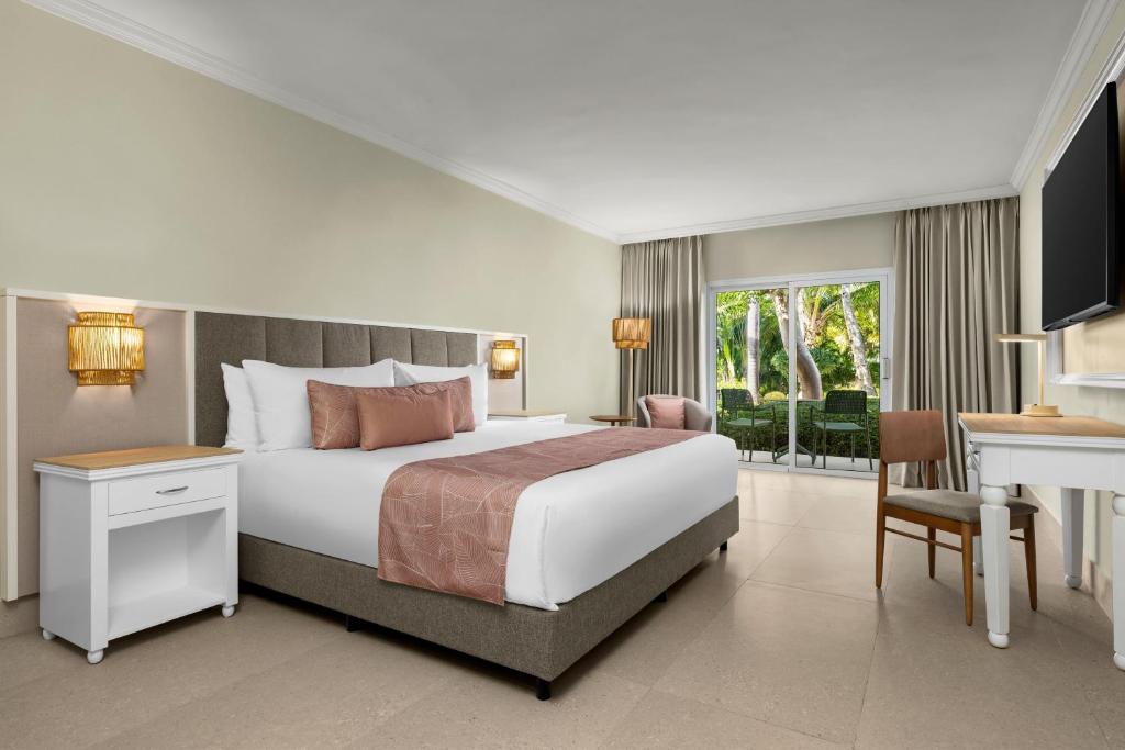 Quarto do Wyndham Alltra Punta Cana All Inclusive Resort, com cama king, detalhes rosados e varanda com vista para o jardim