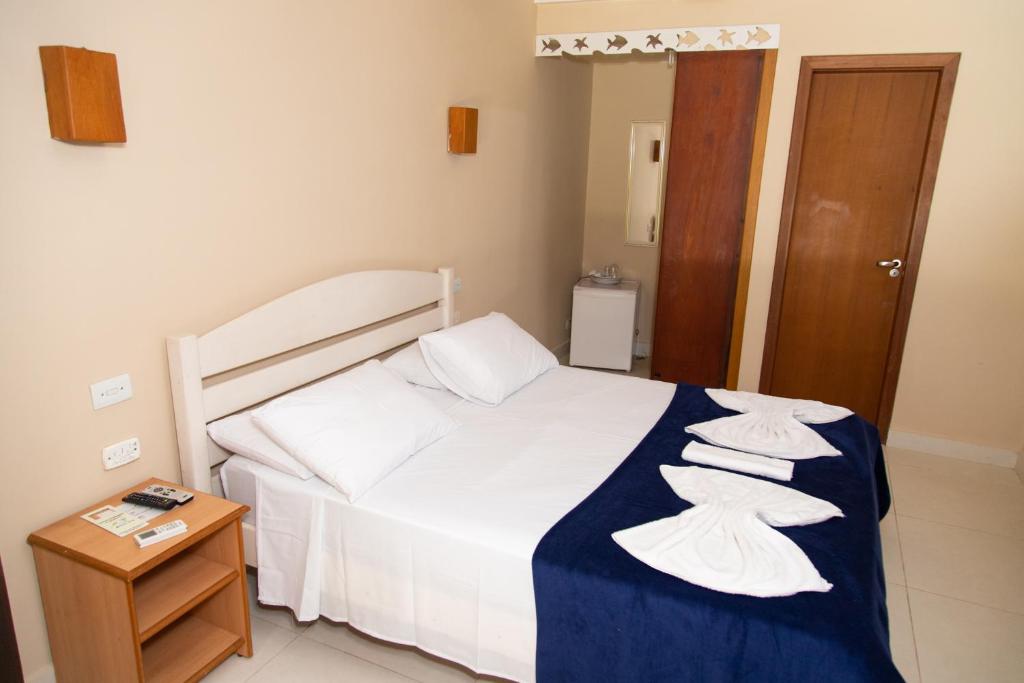 Quarto do Arco Íris Chalé I, em Maresias, com cama branca, manta azul e toalhas dobradas