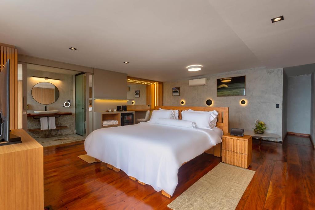 Quarto do Duke Beach Hotel Maresias, em Maresias, com cama branca, piso de madeira e banheiro integrado