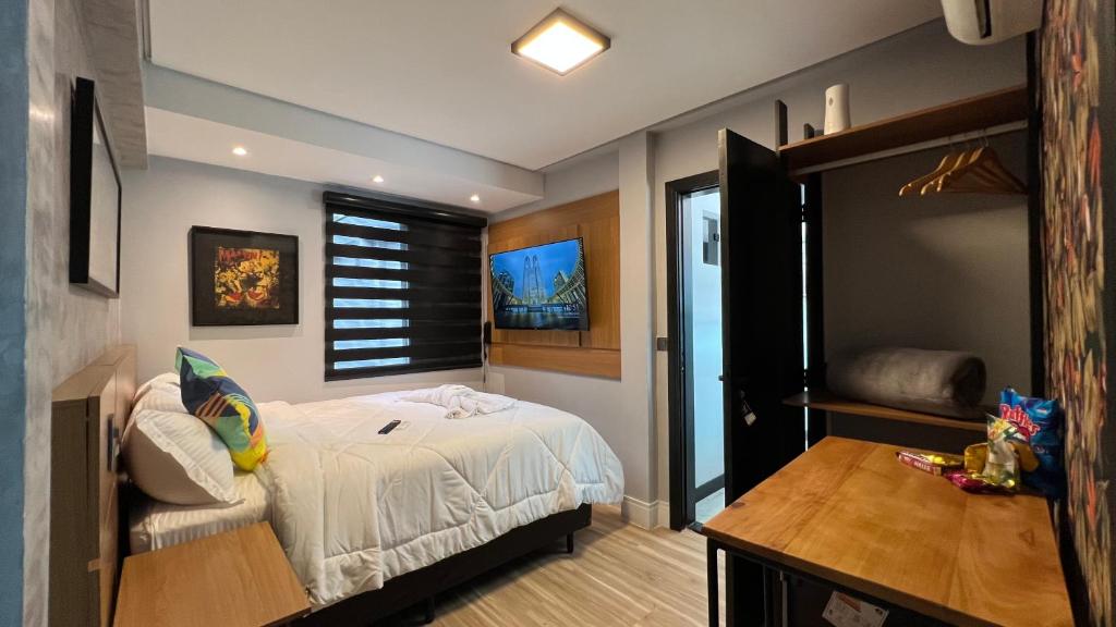 Quarto do Hotel La Serena, em Maresias, com cama branca, TV na parede e armário aberto