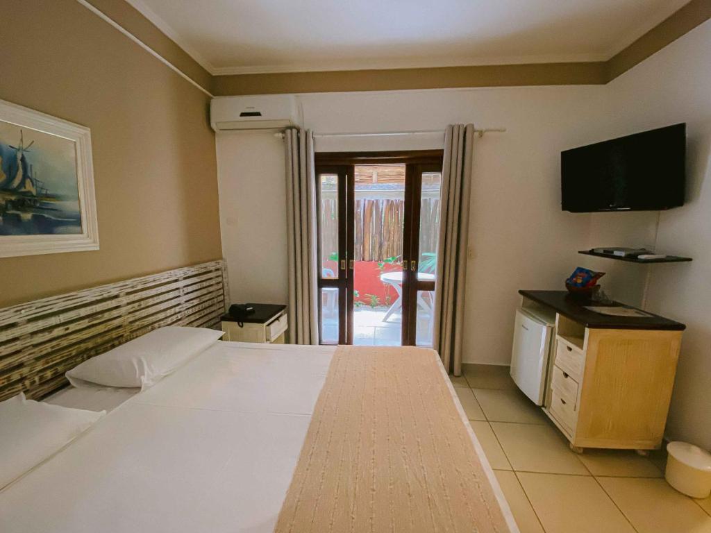 Quarto da Pousada Porto Mare, em Maresias, com cama branca, porta de vidro para área externa e TV na parede