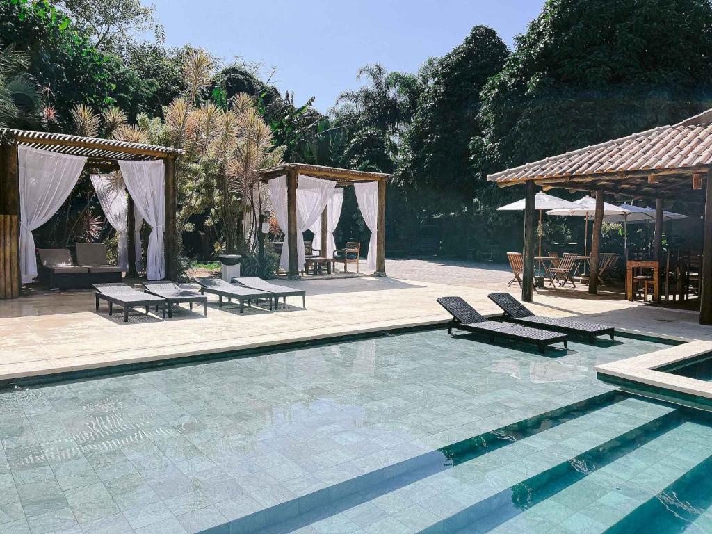 Área da piscina da Pousada Porto Mare, em Maresias, com cabanas, espreguiçadeiras e vegetação ao redor