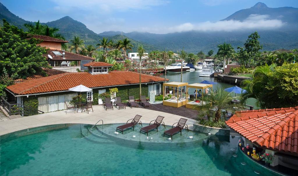 Área externa do Angra Boutique Hotel, com piscina, espreguiçadeiras, marina e montanhas ao fundo