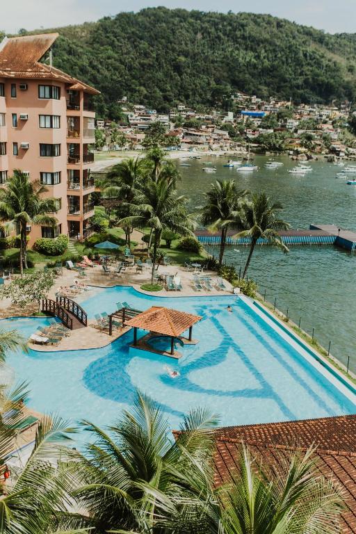 Área externa do Hotel Nacional Inn Angra dos Reis, com piscina diante da baía e morros cobertos por casas