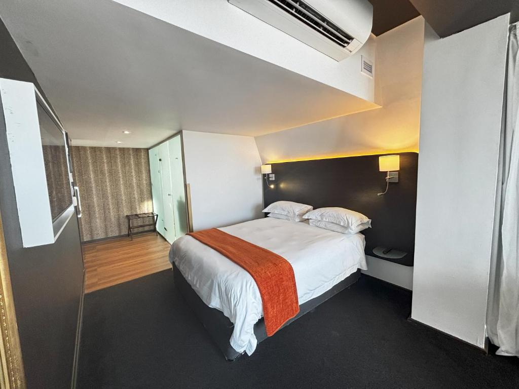 Quarto do ONOMO Hotel Waterfront, com cama de casal, manta laranja e cabeceira preta