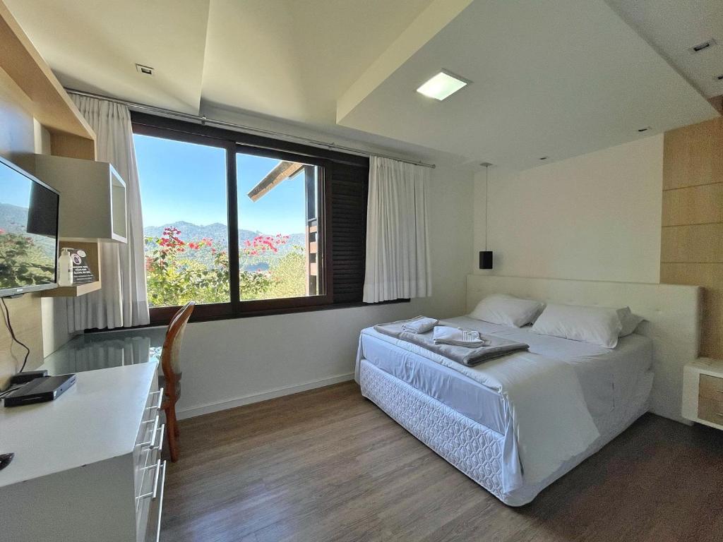 Quarto da Casa Branca Pousada, em Pomerode, com cama de casal e janela voltada para as montanhas.