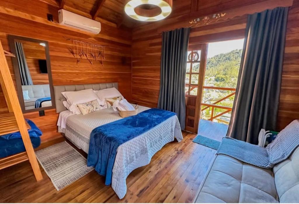Quarto da Pousada Hoff Haus, em Pomerode, com revestimento de madeira, cama de casal e varanda com vista para as montanhas.