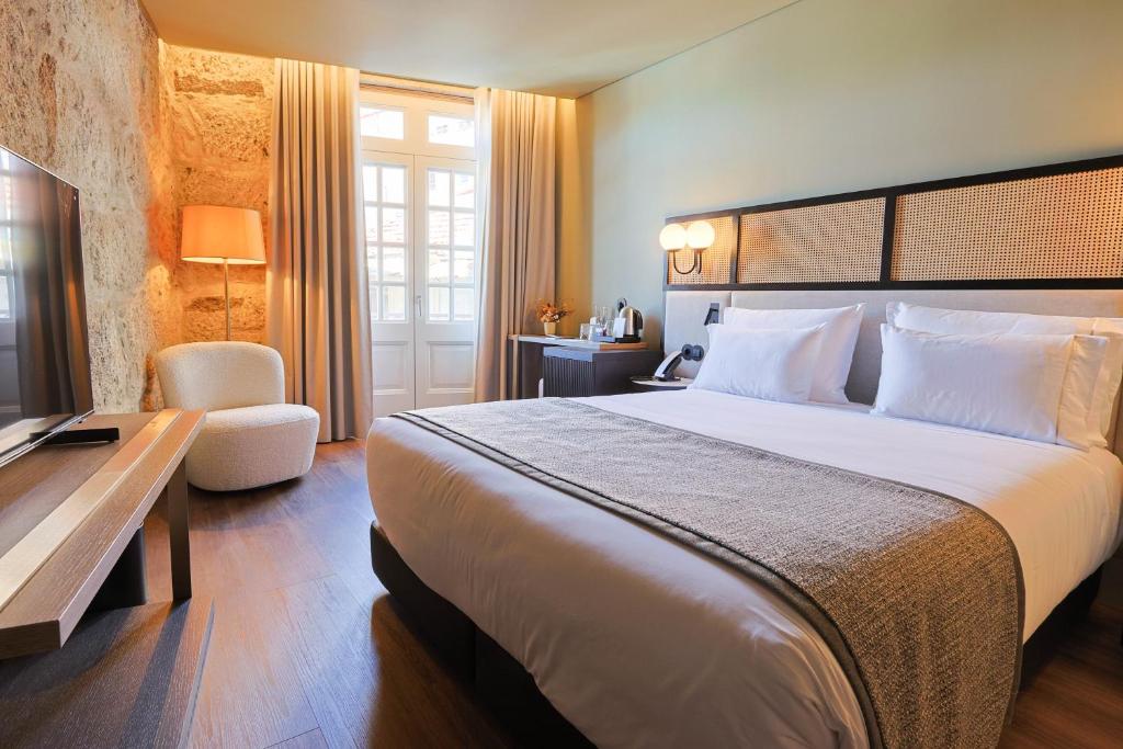 Quarto do Timbre Virtudes, no Porto, com cama branca, parede de pedra e poltrona clara