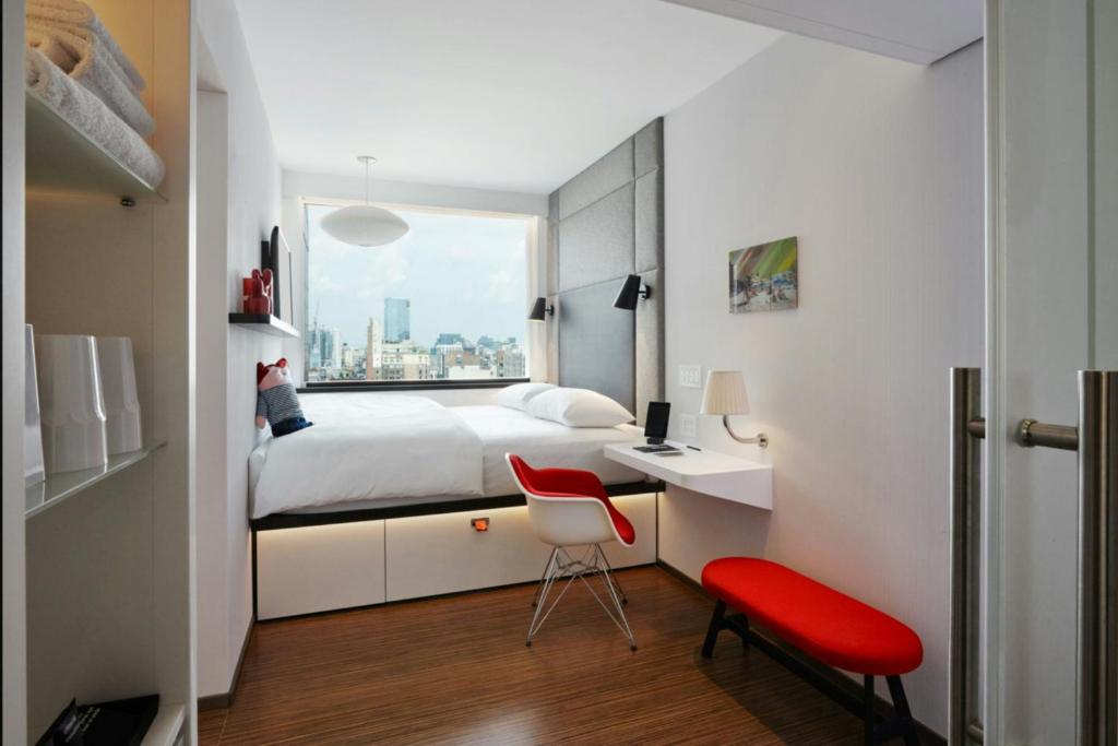 Quarto compacto do citizenM New York Bowery, em Nova York, com cama junto à janela e móveis vermelhos.
