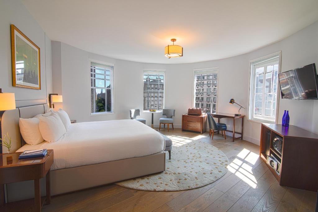 Quarto amplo do Hotel Belleclaire Central Park, em Nova York, com janelas curvas e móveis de madeira.