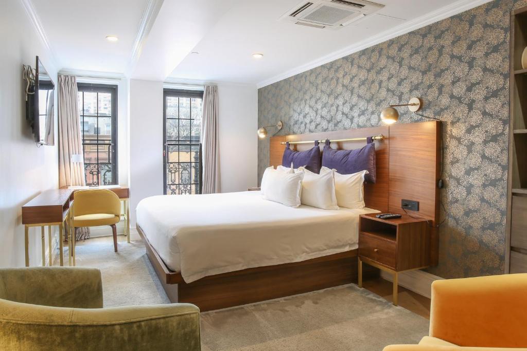 Quarto do Hotel Scherman, em Nova York, com cama de casal, poltronas e papel de parede floral.
