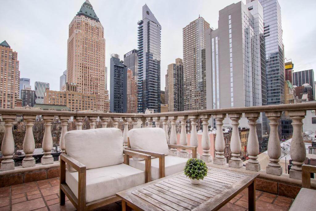 Terraço do Hotel Scherman, em Nova York, com poltronas claras e vista para os prédios de Midtown.