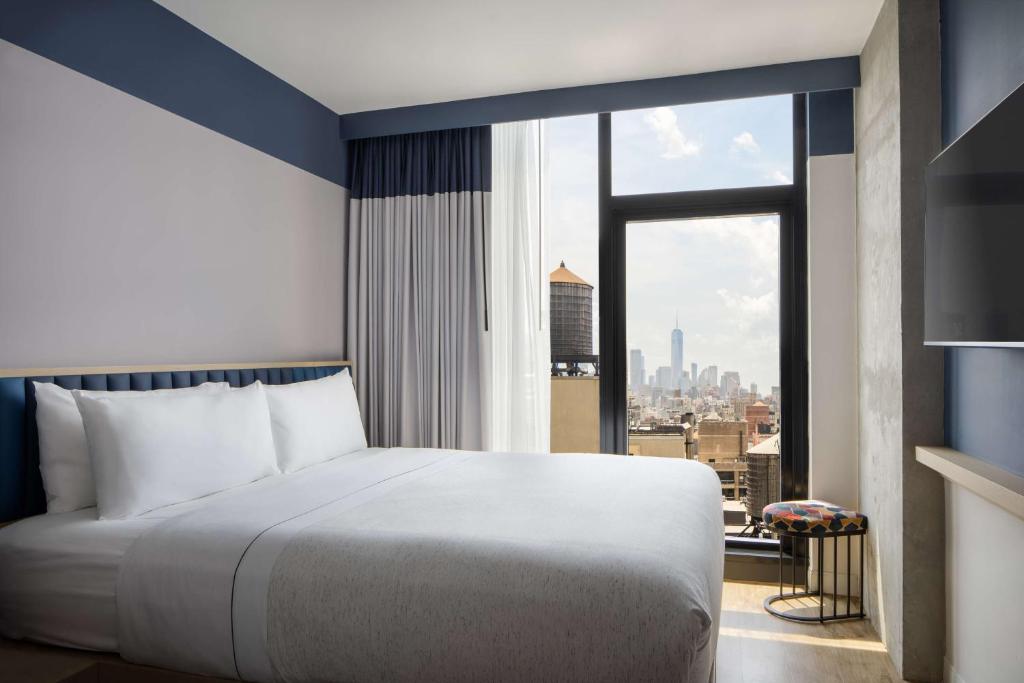 Quarto do Motto by Hilton New York City Chelsea, em Nova York, com cama junto ao janelão e vista para Manhattan.
