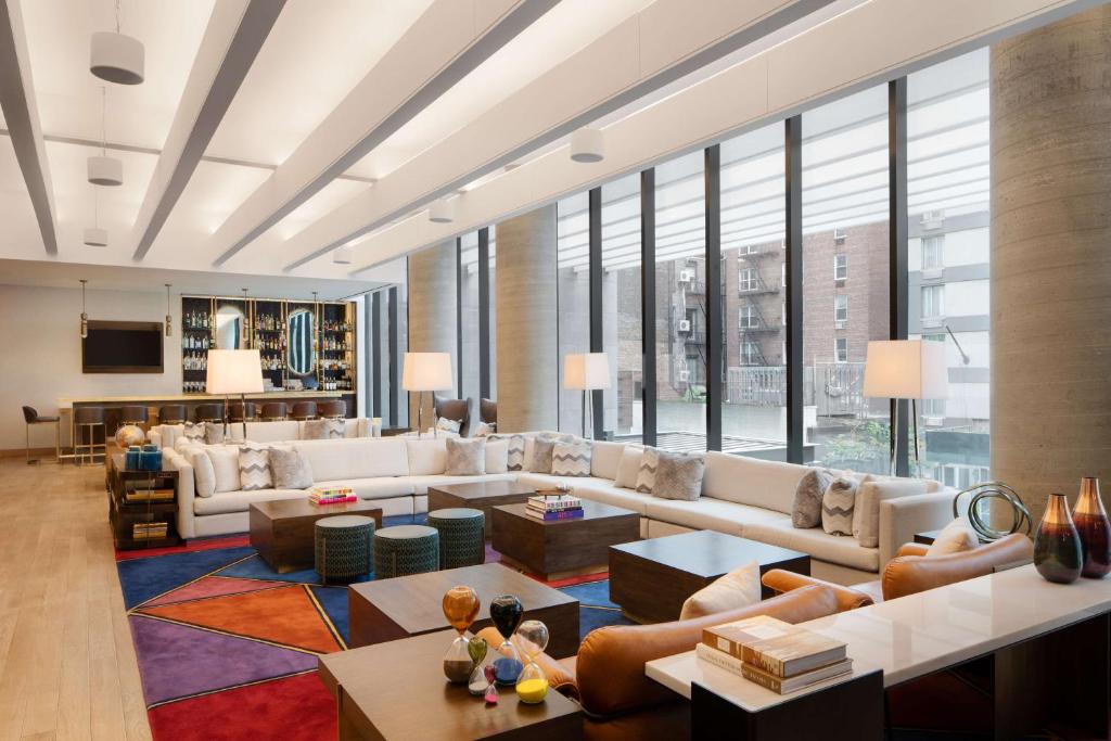 Lounge do Motto by Hilton New York City Chelsea, em Nova York, com sofá branco e janelas amplas.