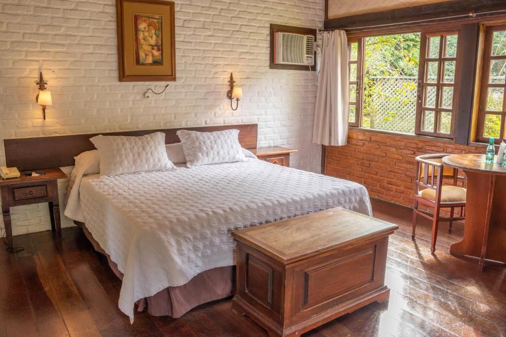 Quarto do Bomtempo Itaipava Hotel by Castelo Itaipava com cama ampla, móveis de madeira e parede de tijolos.