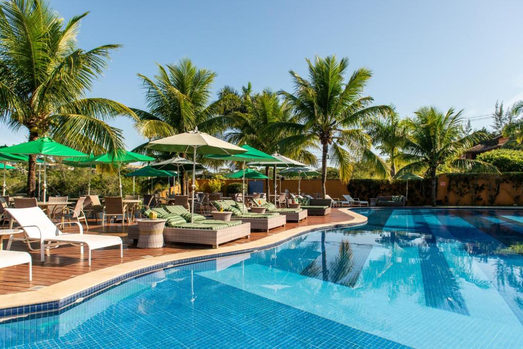 Área de piscina do Hotel Ferradura Resort, em Búzios, com palmeiras, espreguiçadeiras e guarda-sóis verdes.