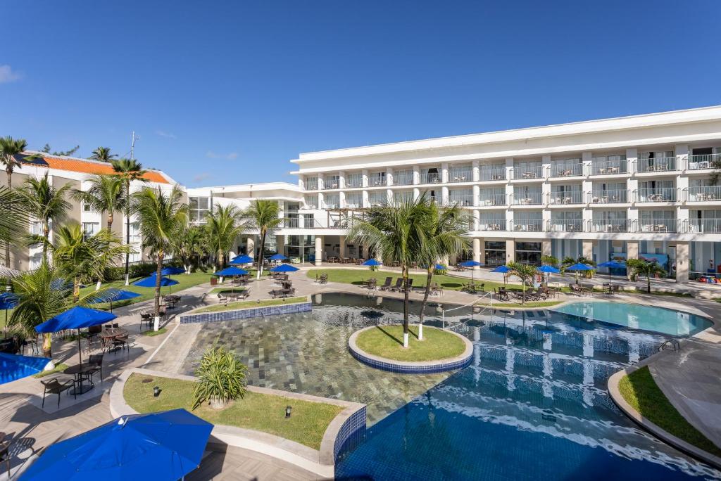 Piscina do Marupiara All Inclusive Resort by Wish, em Porto de Galinhas, com coqueiros e guarda-sóis azuis