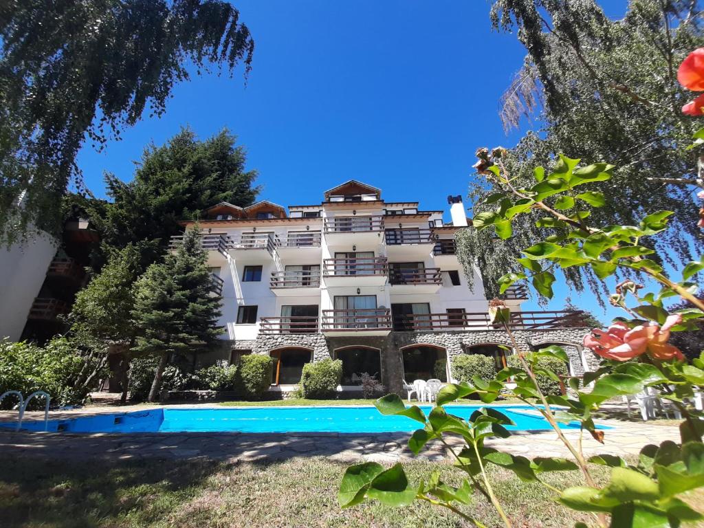Área externa do Apartur Catedral, em Bariloche, com piscina, jardim e edifício cercado por árvores.