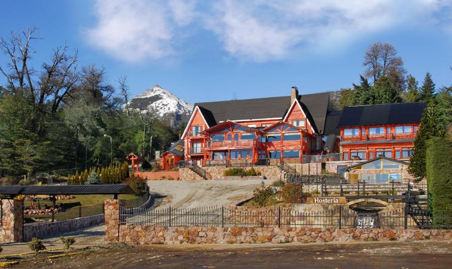 Área comum do La Justina Hostel, em Bariloche, com mesas, sofá e grandes janelas voltadas para o jardim.