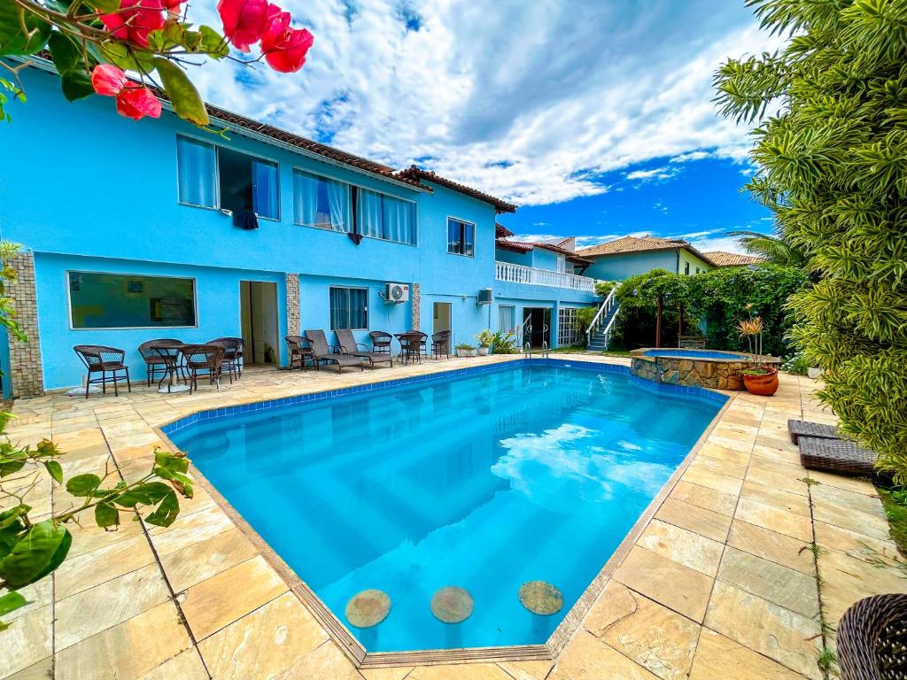 Área da piscina da Ibello Beach Pousada, em Cabo Frio, com fachada azul e mesas ao redor