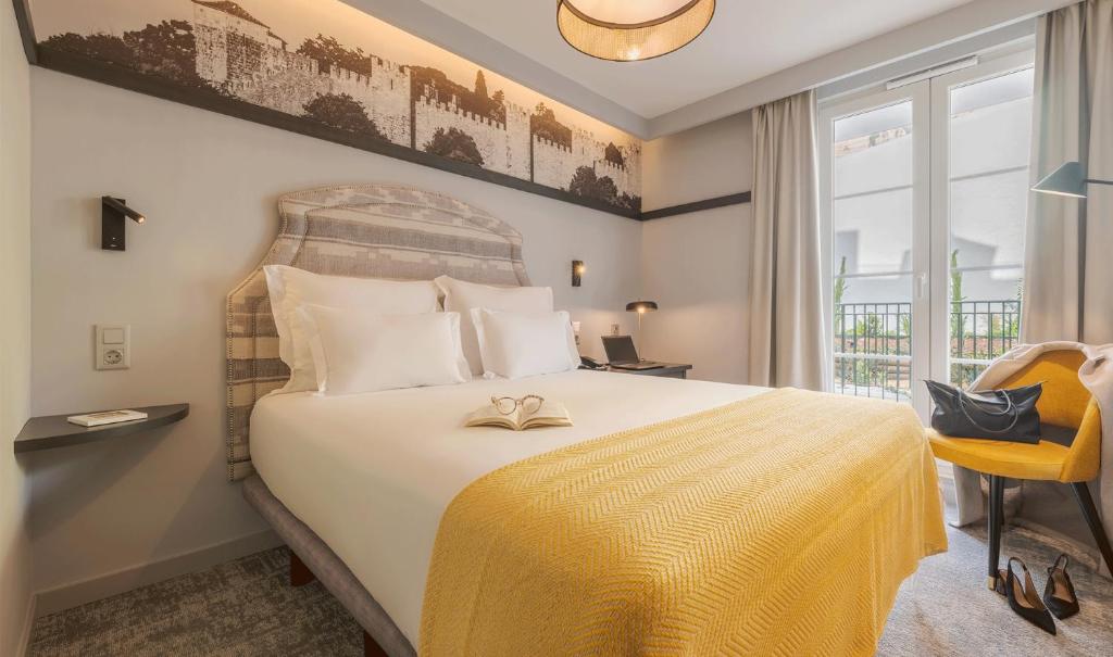 Quarto da Pousada Alfama, em Lisboa, com cama de casal, manta amarela e portas para a varanda.