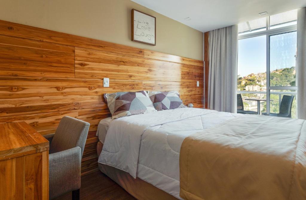 Quarto do Hotel Petrópolis Inn, em Petrópolis, com cama de casal, painel de madeira e varanda.