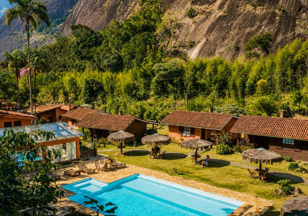 Área externa do Kastel Pedra Bonita, em Petrópolis, com piscina, chalés e montanhas ao redor.