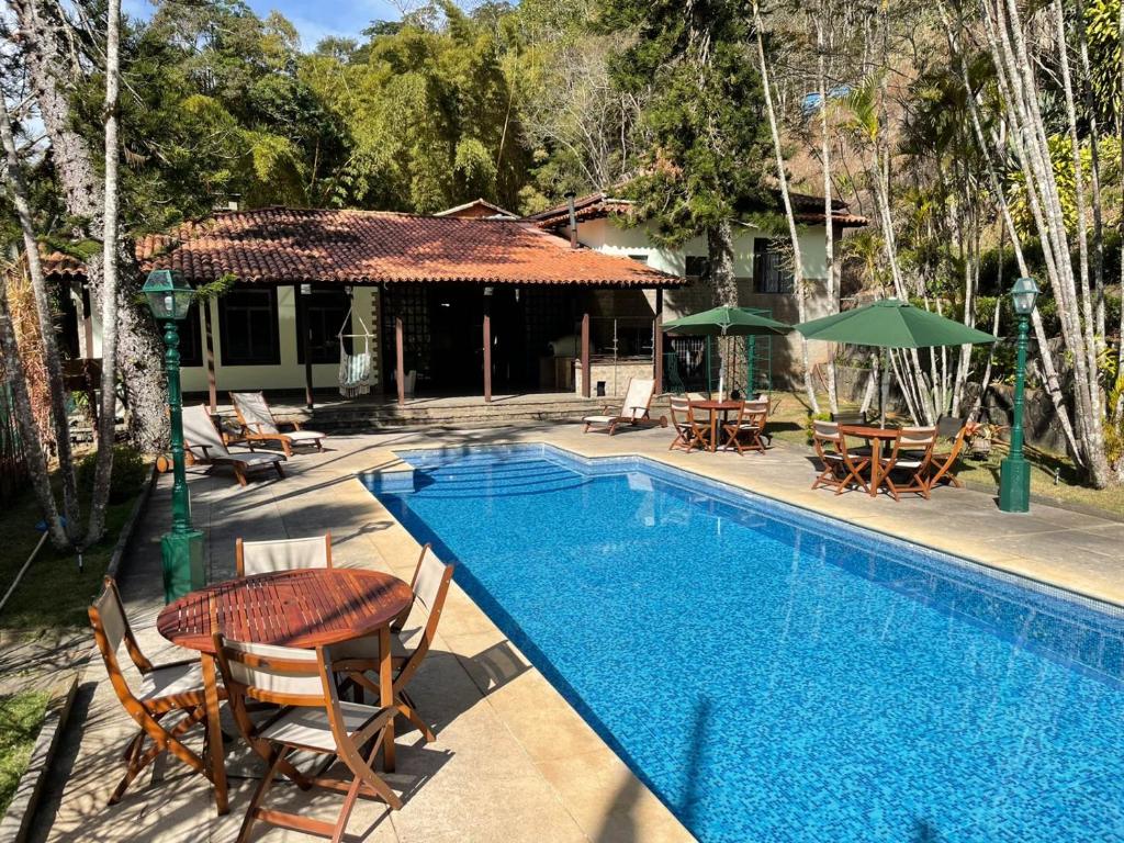 Piscina da Pousada Cozy Home, em Petrópolis, cercada por jardins, mesas ao ar livre e área arborizada.