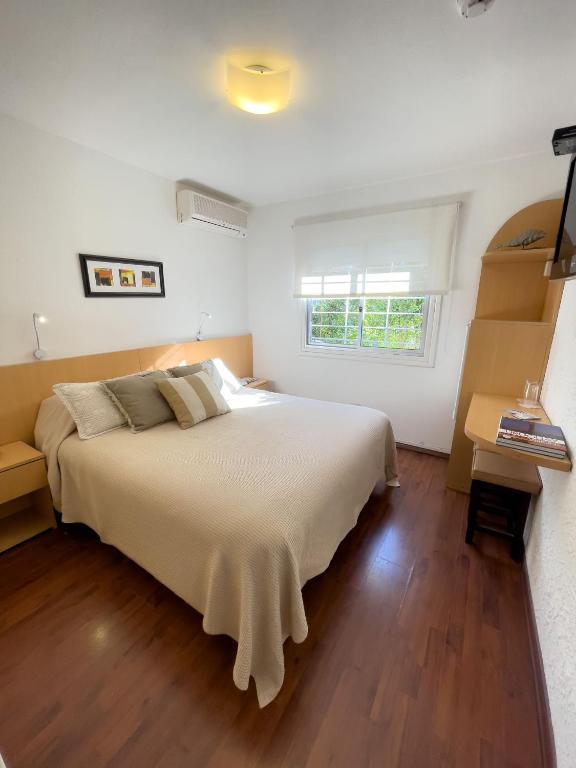 Quarto do Hotel Ajax, em Punta del Este, com cama de casal, piso de madeira e janela voltada para o verde.