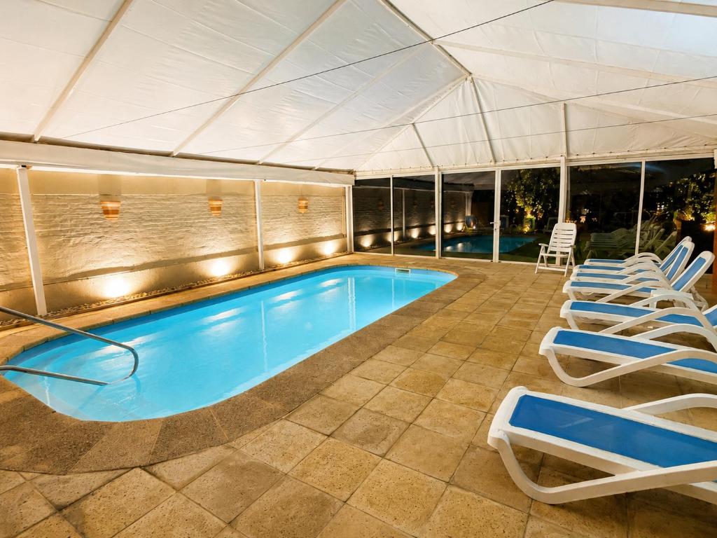Piscina coberta do Hotel Ajax, em Punta del Este, com espreguiçadeiras azuis em uma área fechada e iluminada.