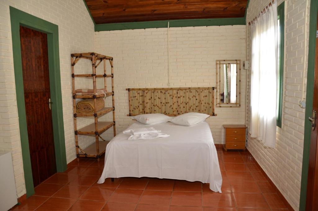 Quarto da Pousada Ecológica Rio do Peixe, em Socorro, com cama de casal, cabeceira de bambu e paredes de tijolos claros.