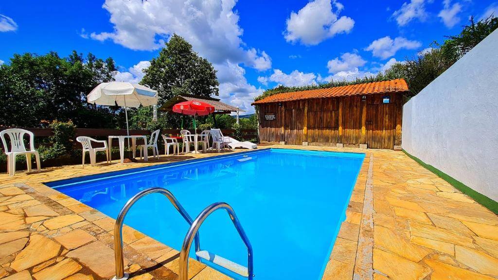 Piscina da Pousada Nativa, em Socorro, com mesas, guarda-sóis e estrutura de madeira ao fundo.