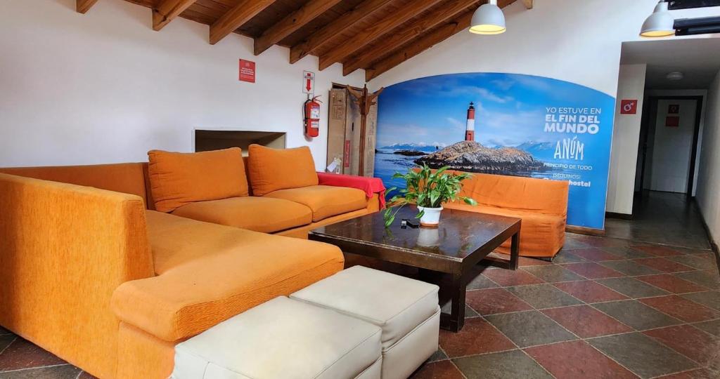 Sala compartilhada do Anum Hostel, em Ushuaia, com sofás laranja e painel do Farol Les Éclaireurs.