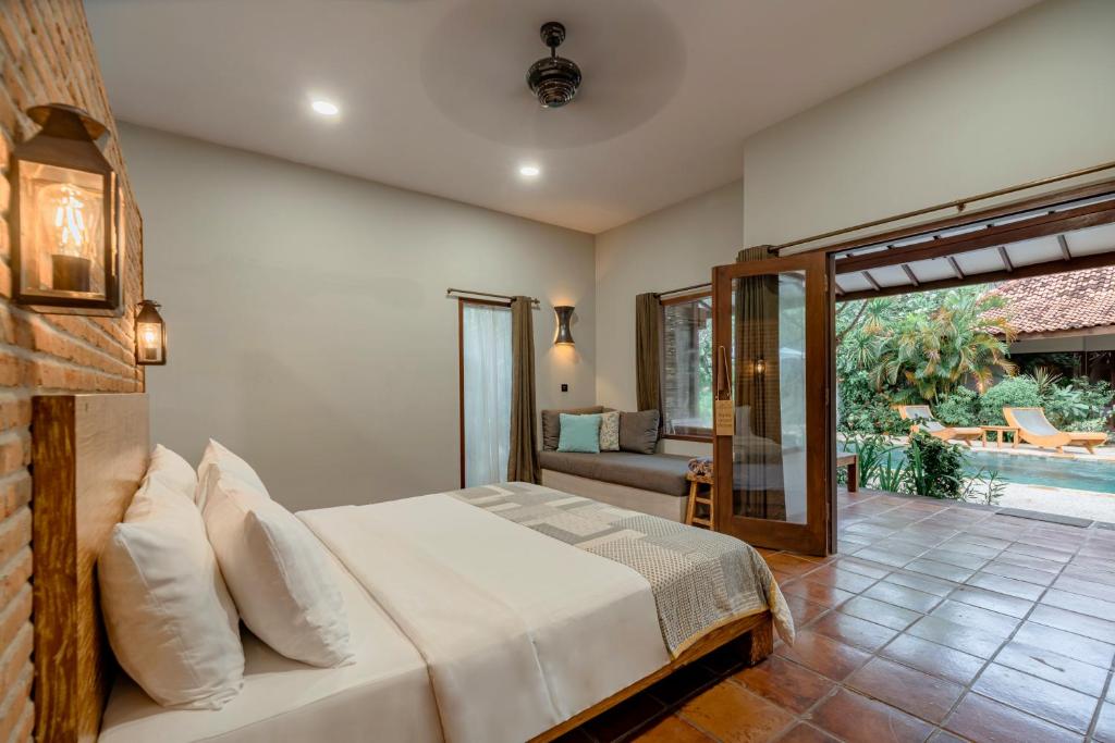 Quarto com cama de casal, parede de tijolos aparentes, porta de vidro aberta e vista para a piscina
