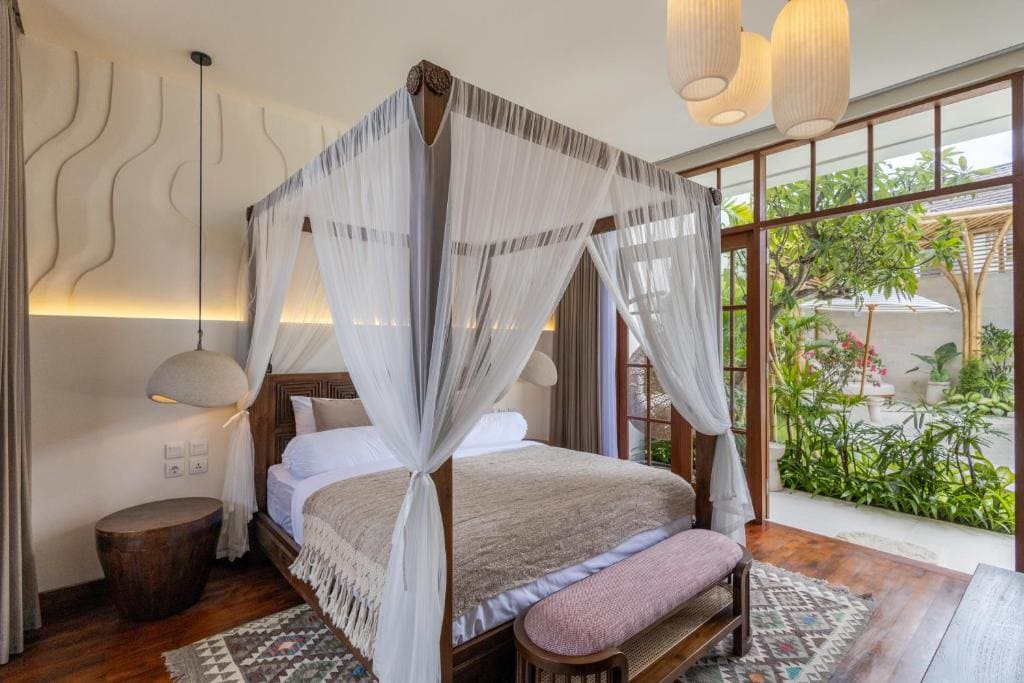 Quarto com cama de dossel, cortinas de voile, piso de madeira e portas de vidro voltadas para o jardim