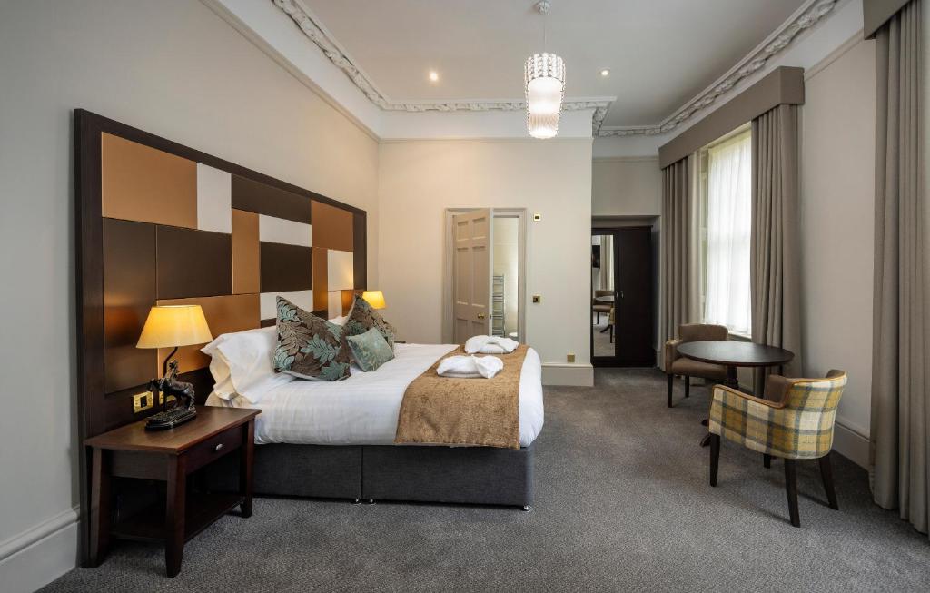 Quarto amplo e elegante com cabeceira de madeira com painéis e poltrona xadrez no Albany Hotel.
