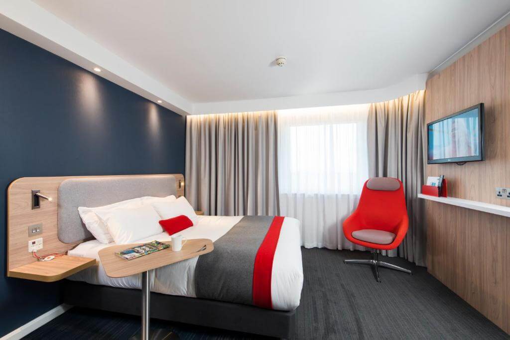 Quarto de hotel contemporâneo no Holiday Inn Express Edinburgh Royal Mile, com cama queen, poltrona vermelha e escrivaninha.