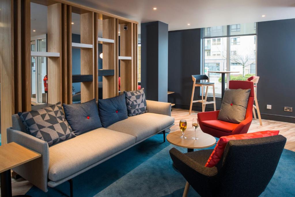 Sala de estar moderna no Holiday Inn Express Edinburgh Royal Mile, com sofá cinza, poltronas coloridas e divisória de madeira.