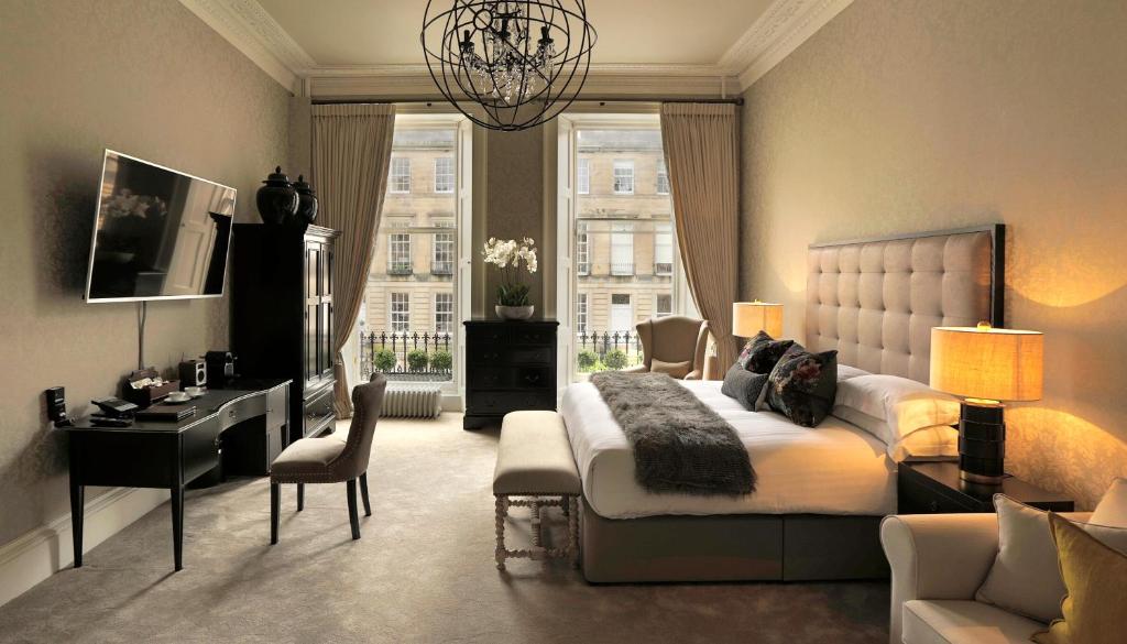 Suíte luxuosa com grandes janelas, cama de casal com cabeceira capitonê e lustre no Nira Caledonia.