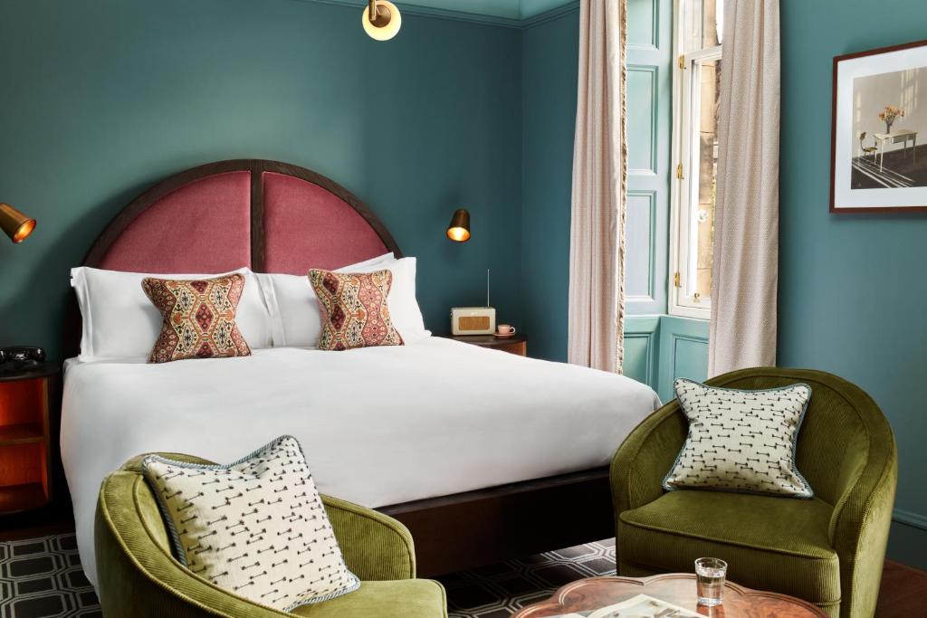 Quarto elegante com paredes azuis, cabeceira arredondada de veludo rosa e poltronas verdes no The Hoxton, Edinburgh.