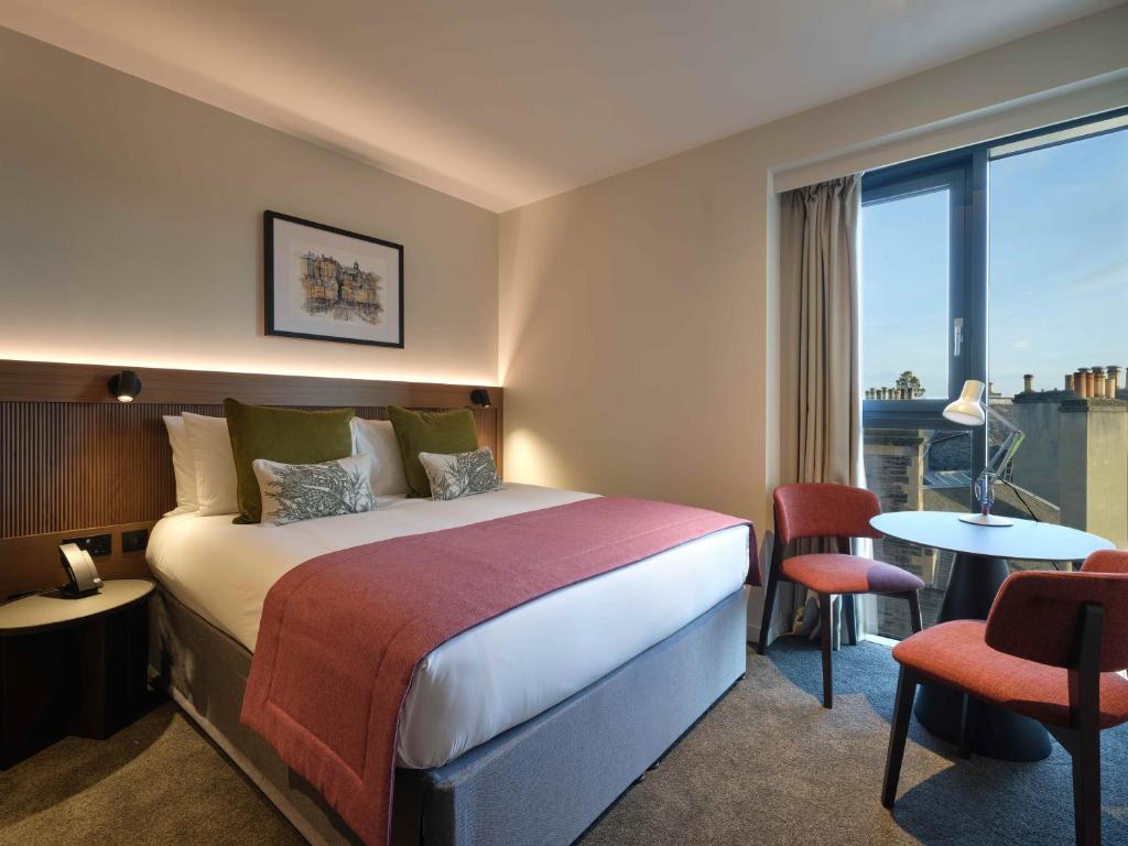 Quarto iluminado com cama de casal, almofadas verdes e cadeiras com mesa junto à janela no The Resident Edinburgh.
