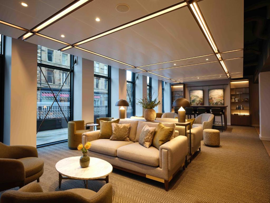 Lounge requintado com sofás cinza, iluminação embutida no teto e poltronas verdes no The Resident Edinburgh.