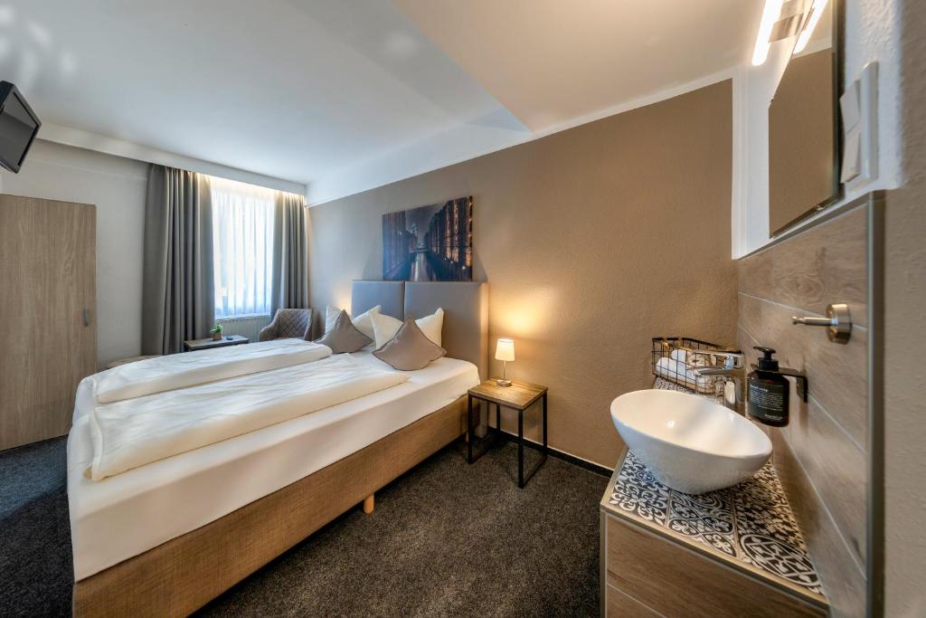 Quarto de hotel confortável com cama de casal arrumada e bancada moderna com pia integrada em Hamburgo.