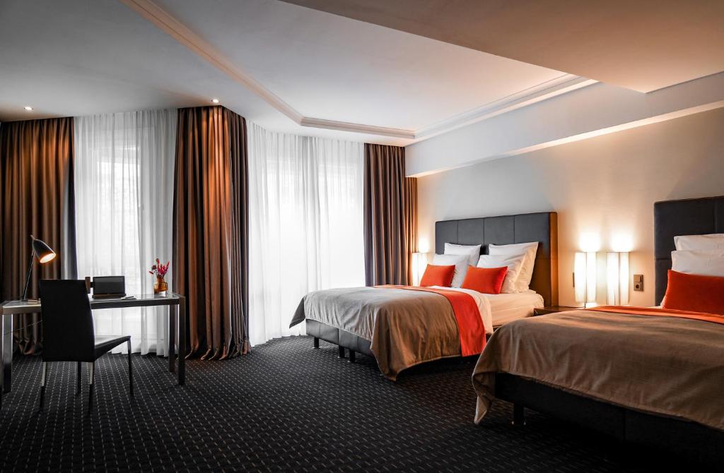 Quarto duplo do Boston Hotel HH com duas camas de casal, detalhes em tom laranja e bancada de trabalho.