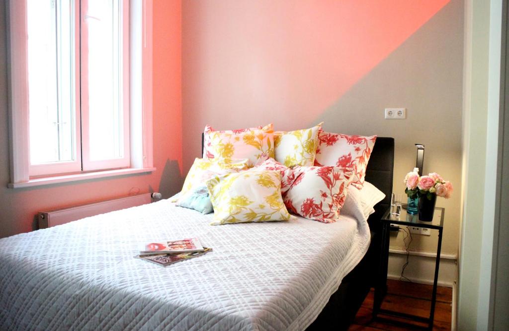 Quarto do Central-Hotel Bel-Etage com parede rosa e cinza, iluminação aconchegante e cama arrumada com almofadas florais.