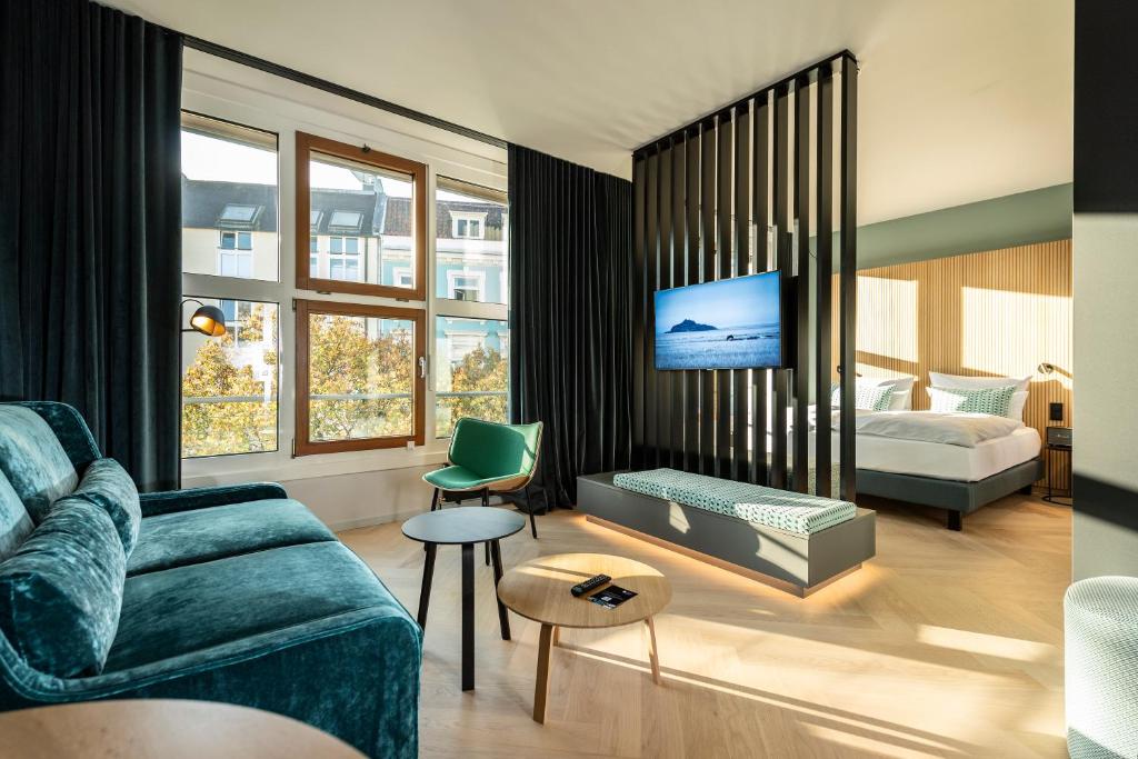 Sala e quarto integrados em um apartamento moderno com sofá verde de veludo, divisória de ripas de madeira e televisão central em Hamburgo.