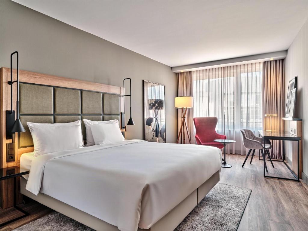 Quarto do Radisson Blu Hotel Hamburg Airport com cama de casal aconchegante, mesa de trabalho e janela com cortinas claras.