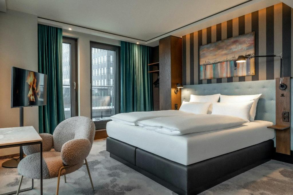 Quarto moderno do The Cloud One Hamburg-Kontorhaus com cama ampla, cortinas azuis e quadro decorativo na parede listrada.
